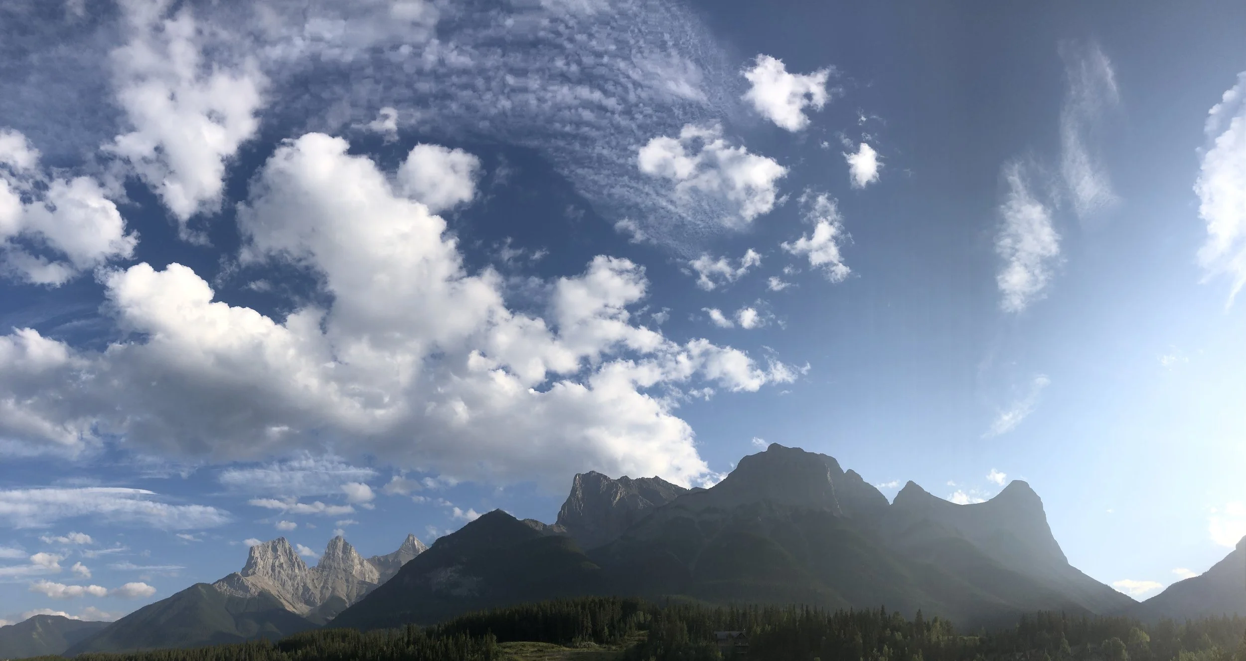 Mountain range with jagged peaks under a blue sky filled with scattered white clouds.