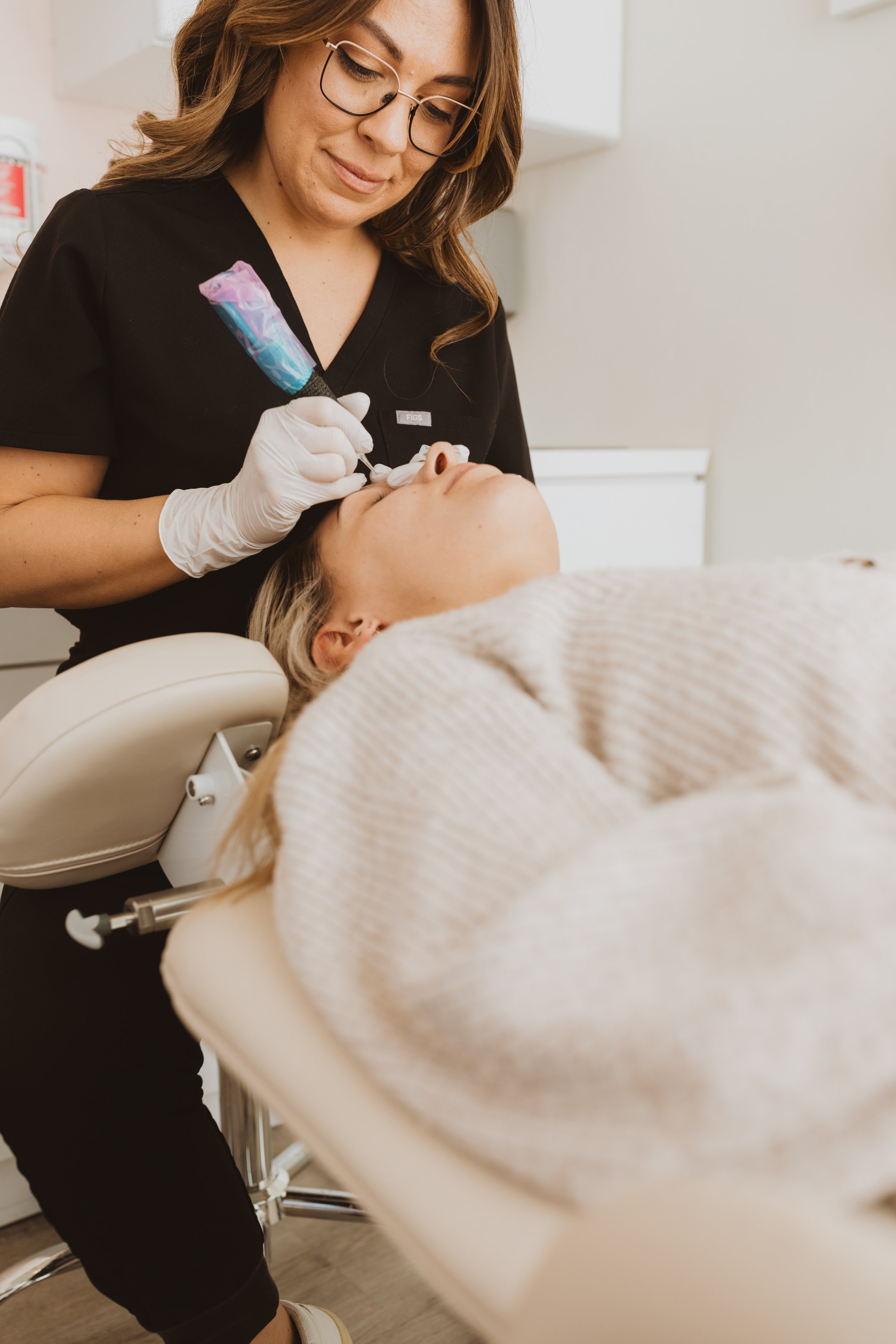 A dentist is performing a procedure on a patient lying in a dental chair. The dentist wears gloves and glasses, and holds dental tools near the patient's mouth.