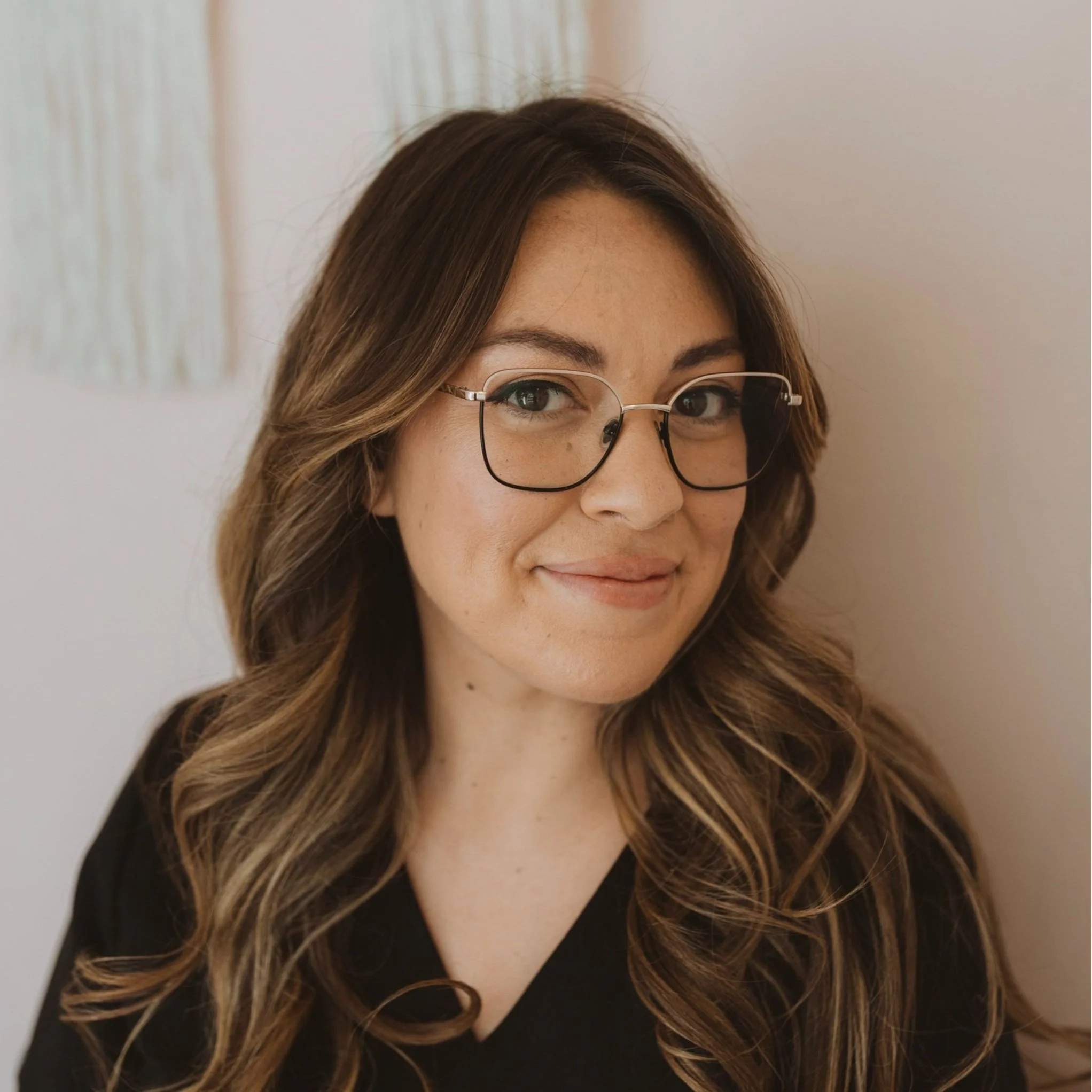 Michelle with brown, wavy hair wearing glasses and a black top, smiling at the camera.