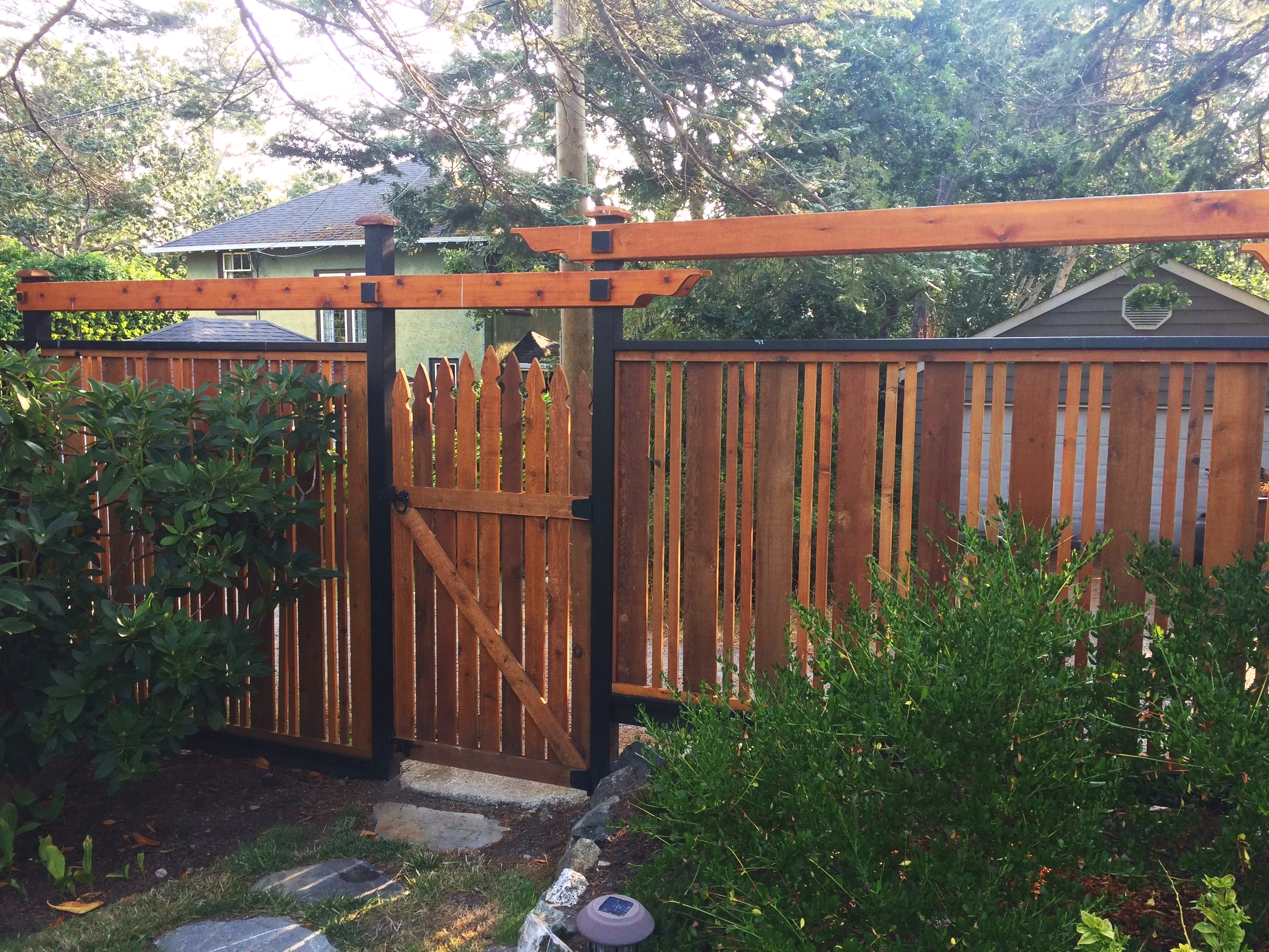 A wooden fence with a gate, surrounded by greenery, in a residential backyard.