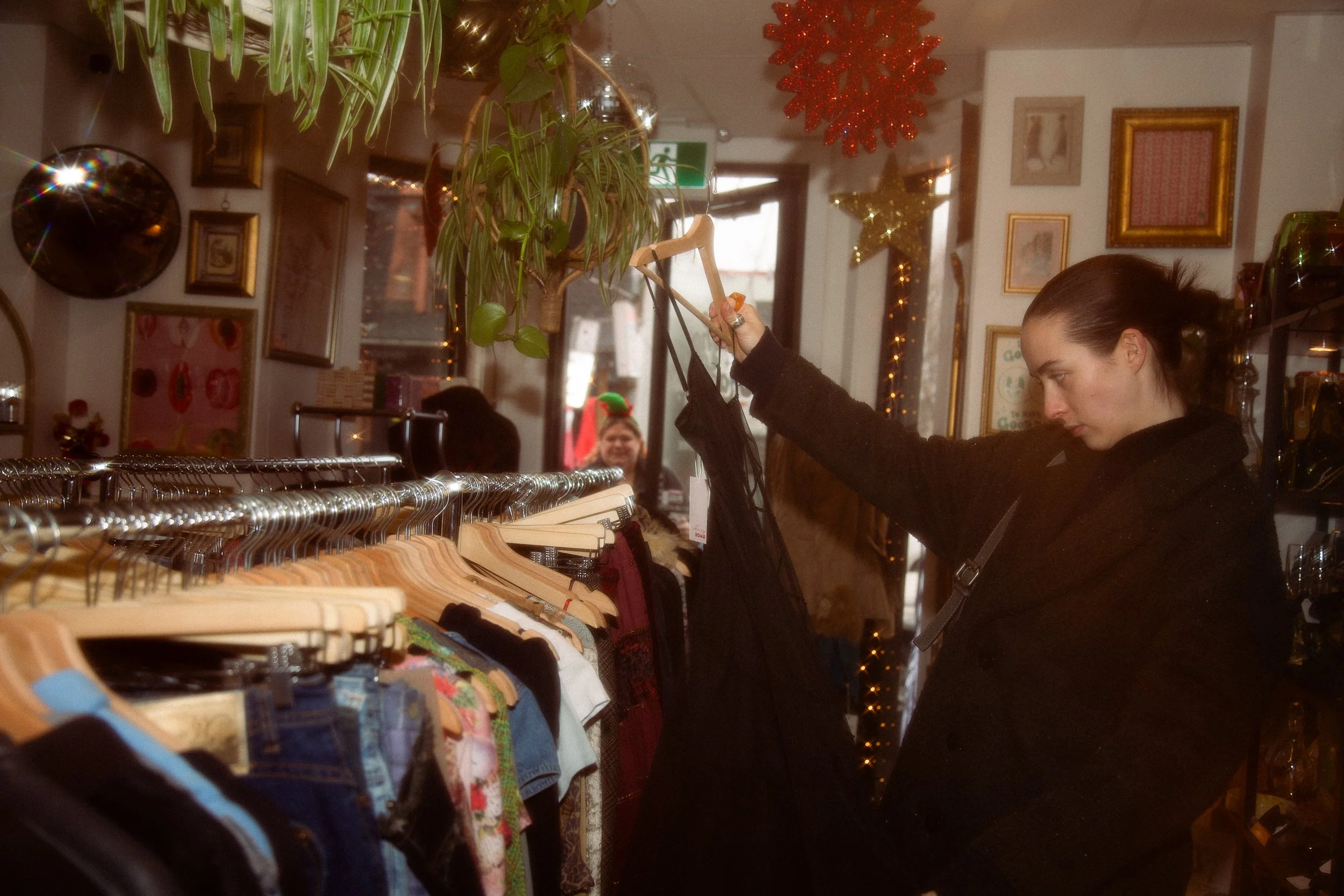 A woman shopping for clothes in a boutique, with Christmas decorations and framed pictures on the wall behind her.