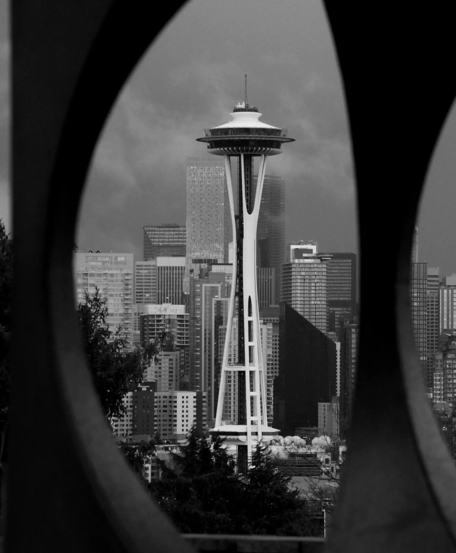 View of the Seattle Space Needle through a framed opening with trees and city buildings in the background.