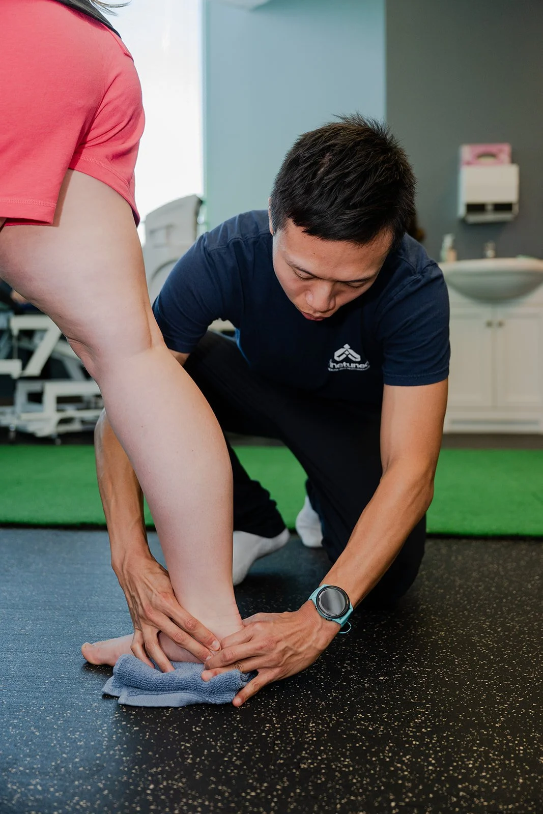 A physical therapist assisting a woman with ankle stretching exercises in a therapy room.