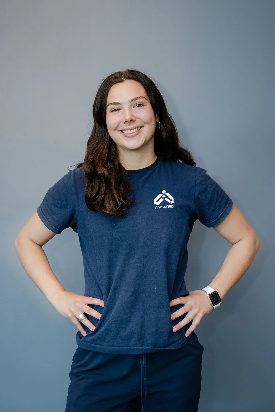 Smiling woman with long dark hair wearing a navy blue fintechunited shirt against a gray background.
