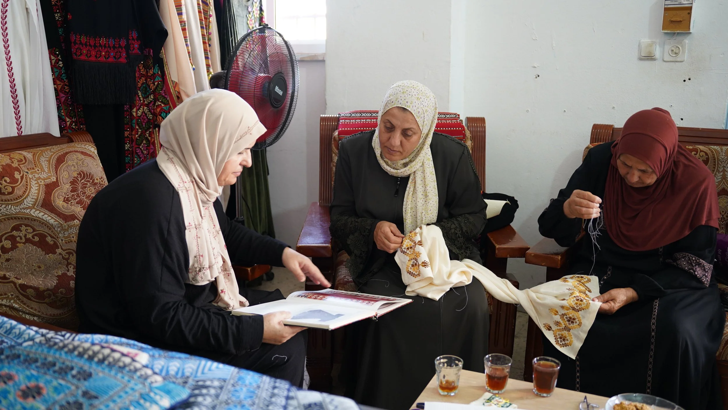 Three Palestinian artisans examining embroidery designs and hand-stitching fabric together at the cooperative in Palestine.