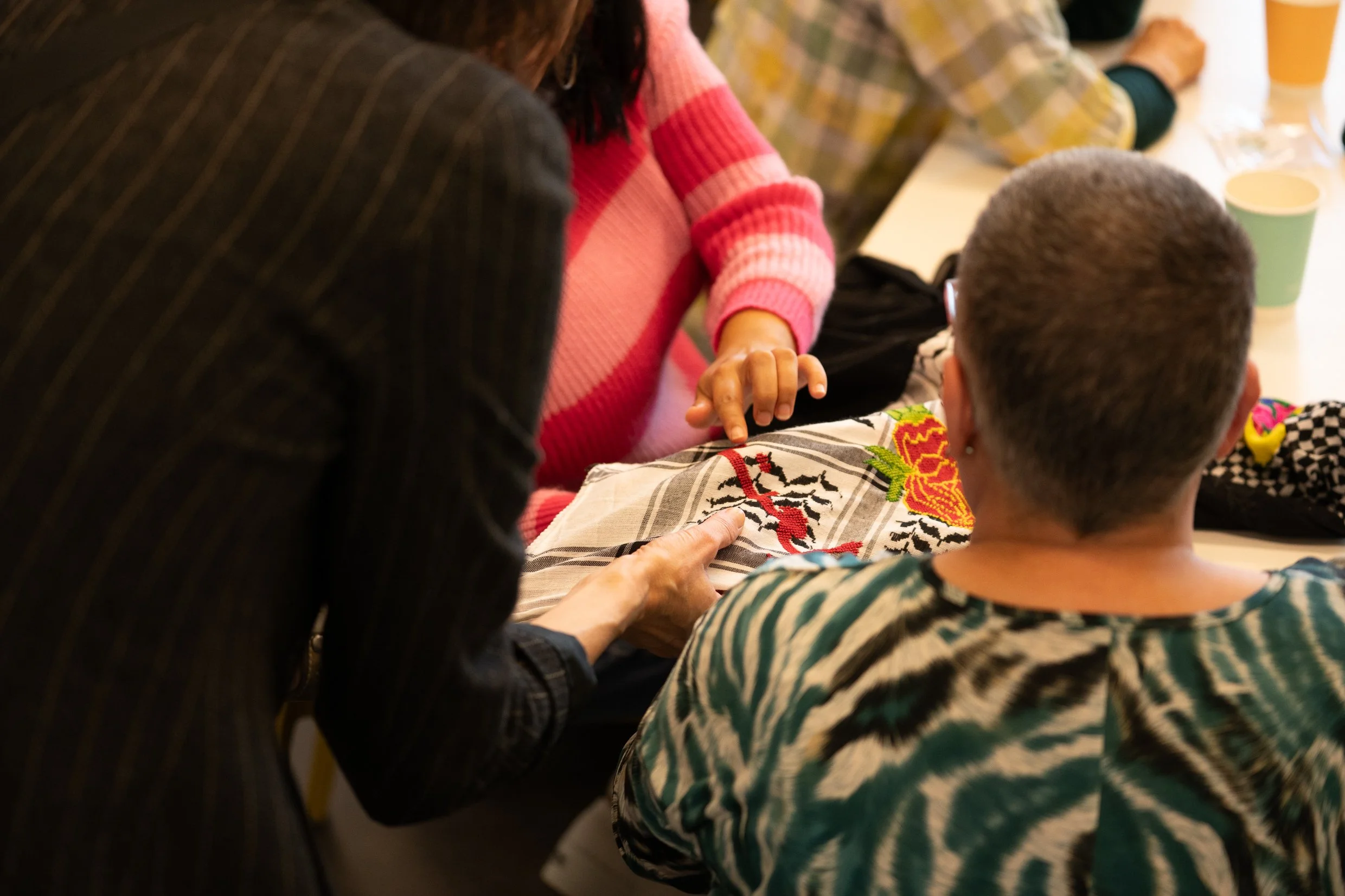 Workshop participants examining colourful Palestinian tatreez embroidery motifs stitched onto fabric.