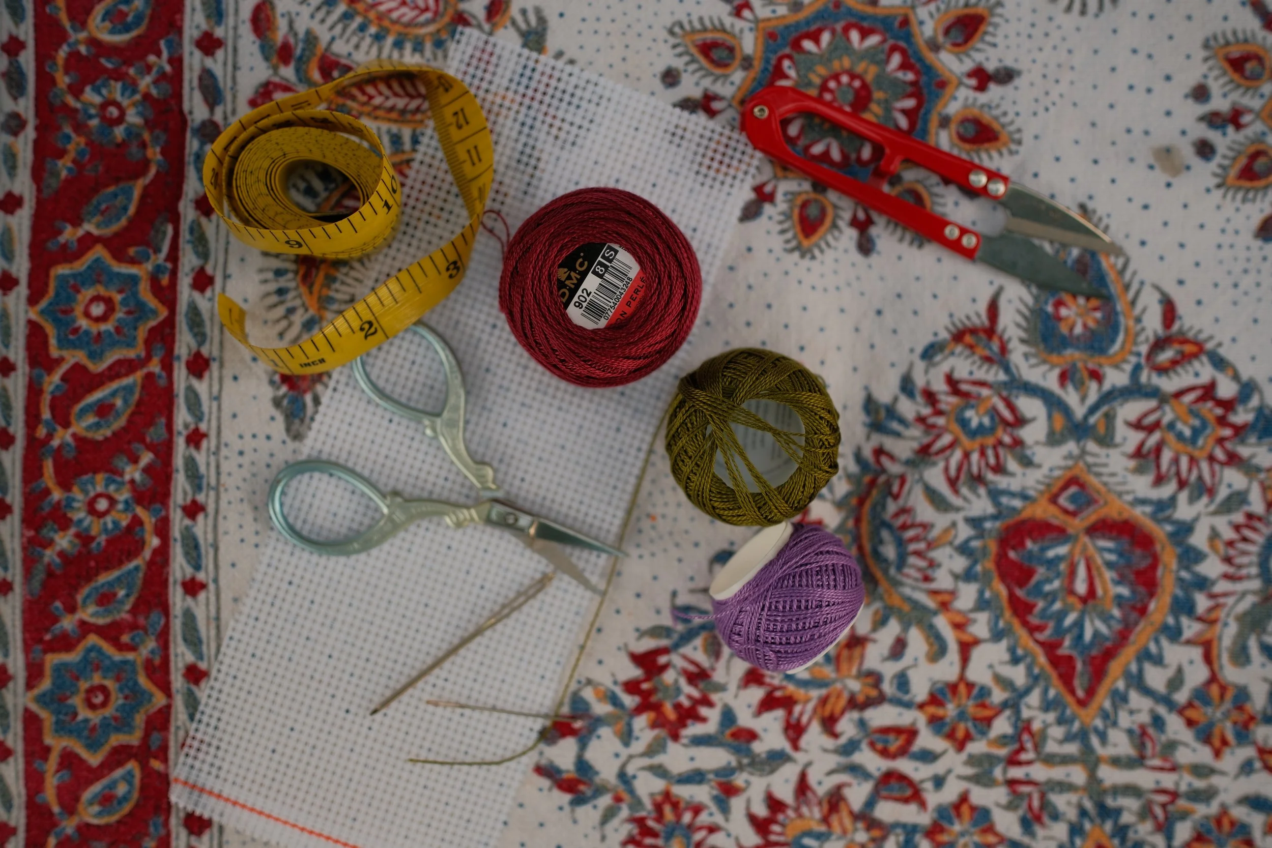 Colourful embroidery threads, Aida fabric, scissors and measuring tape arranged for a Palestinian tatreez workshop.
