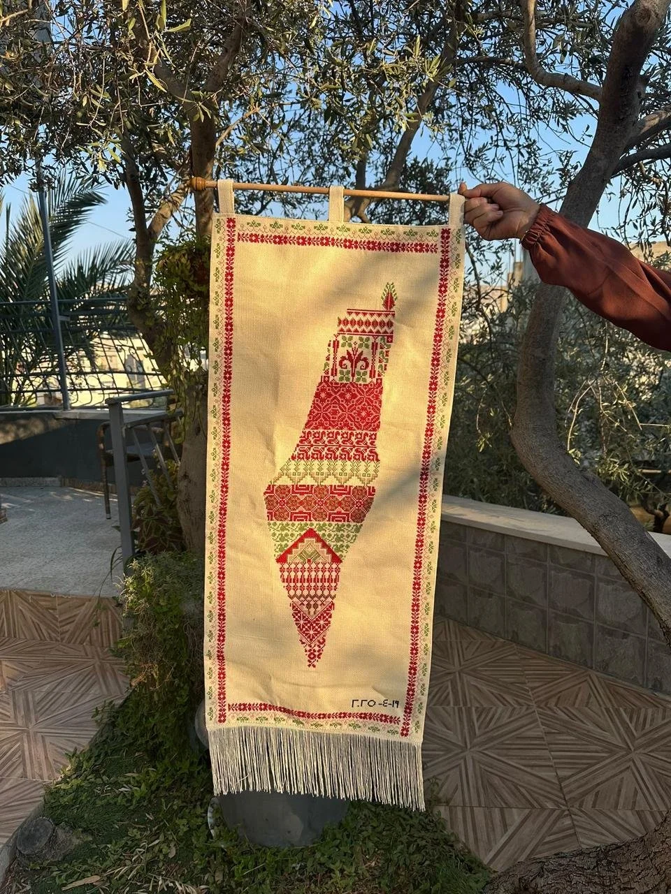 Hand-embroidered map of Palestine in red and green tatreez motifs on a cream wall hanging, personalised with a wedding date and decorative fringe.