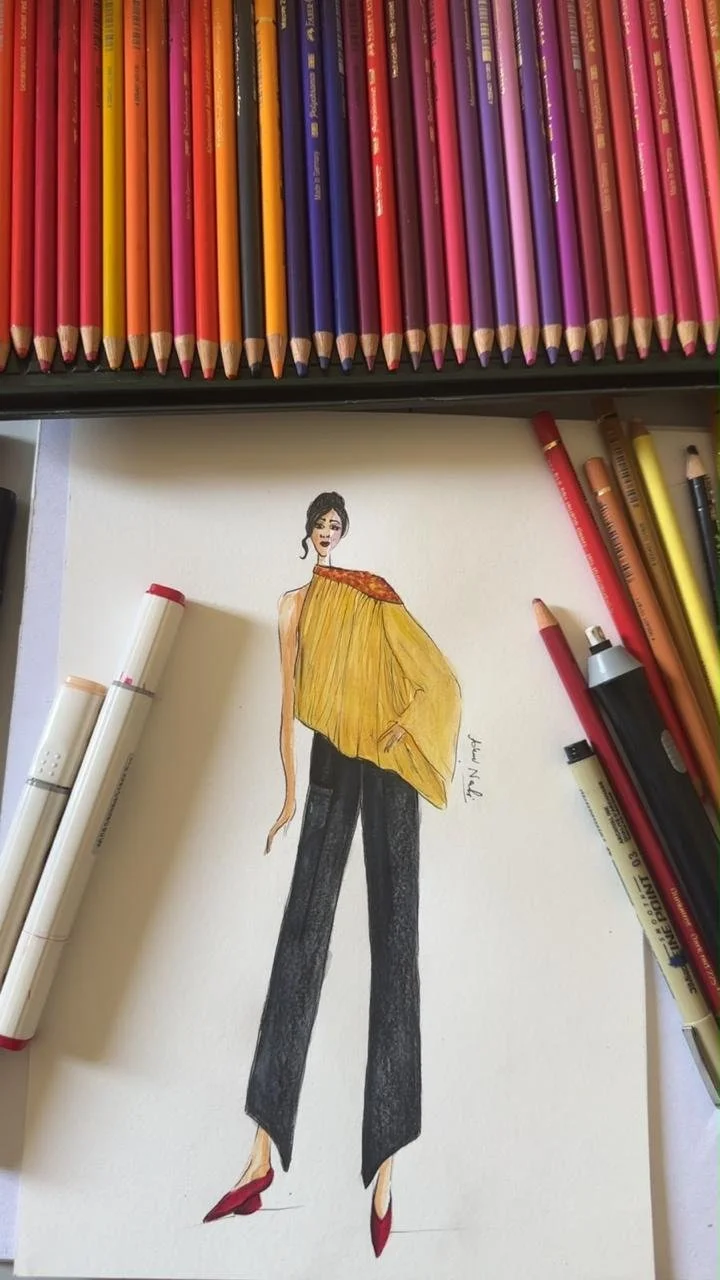 Hand-drawn fashion illustration of a yellow one-shoulder cape top with black wide-leg trousers, surrounded by coloured pencils.
