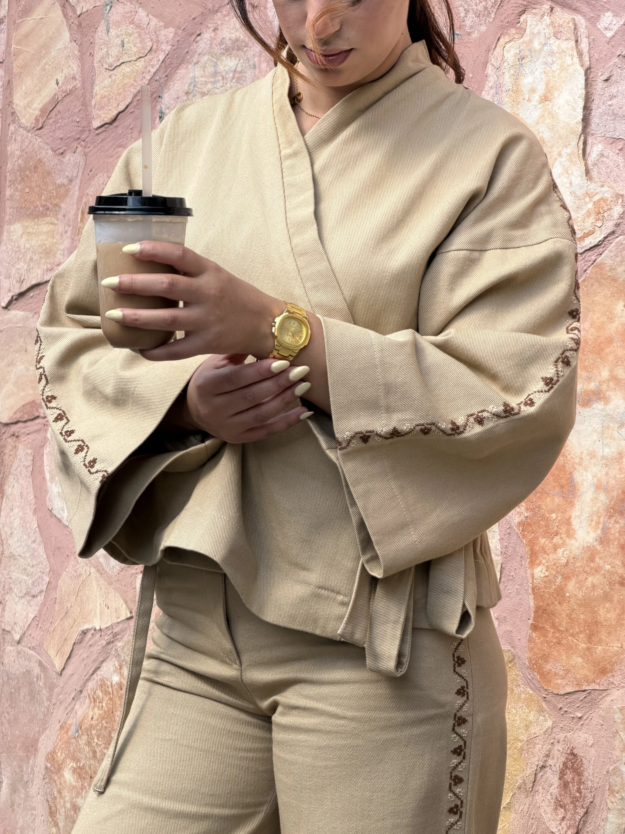 Model wearing the beige Amira Jean Jacket in cotton twill, featuring a wrap-style front, wide sleeves and brown Palestinian tatreez hand embroidery.