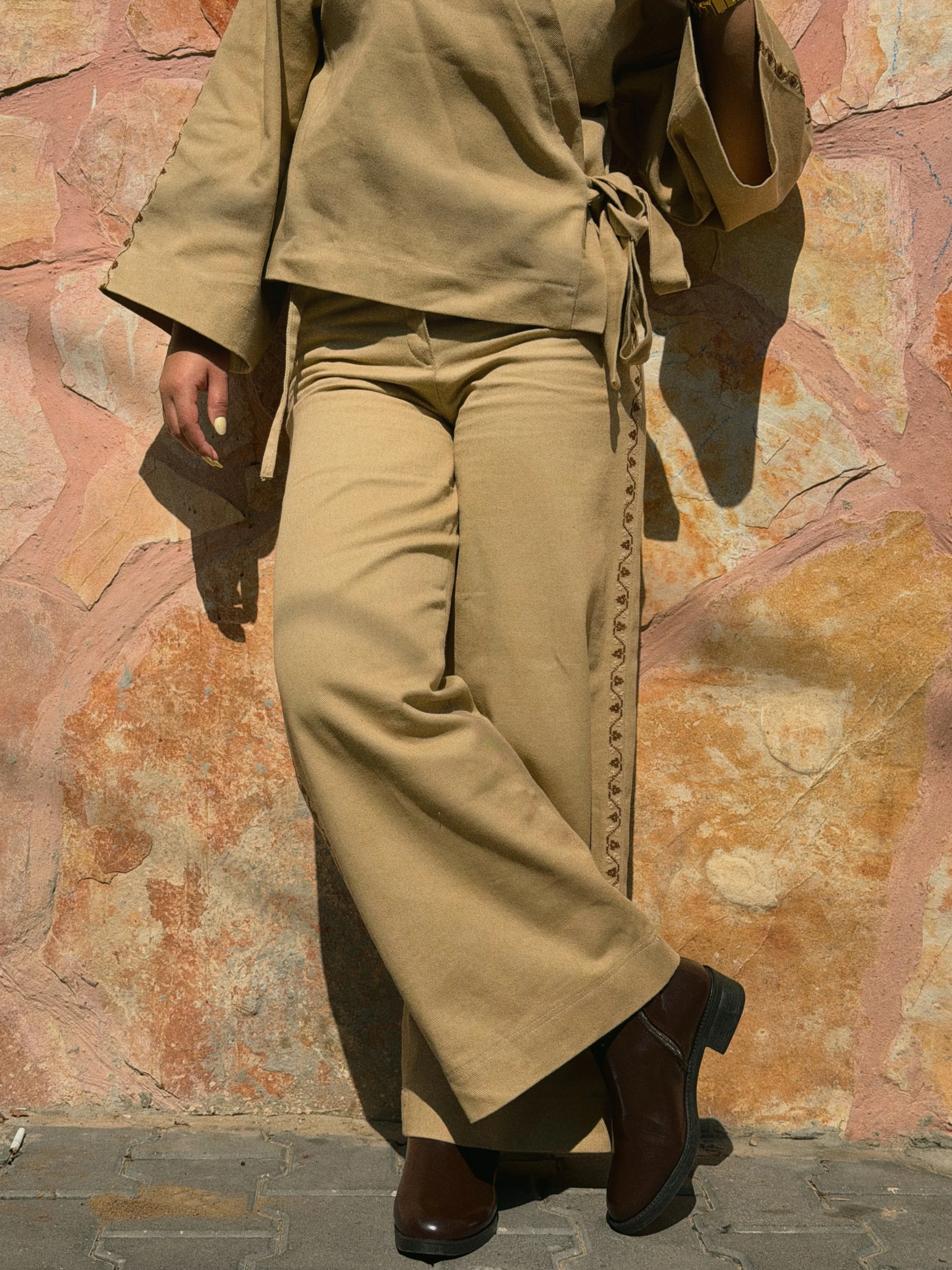 Beige Amira Tatreez Trousers in cotton twill with brown Palestinian hand embroidery along the leg, styled with the matching wrap jacket.