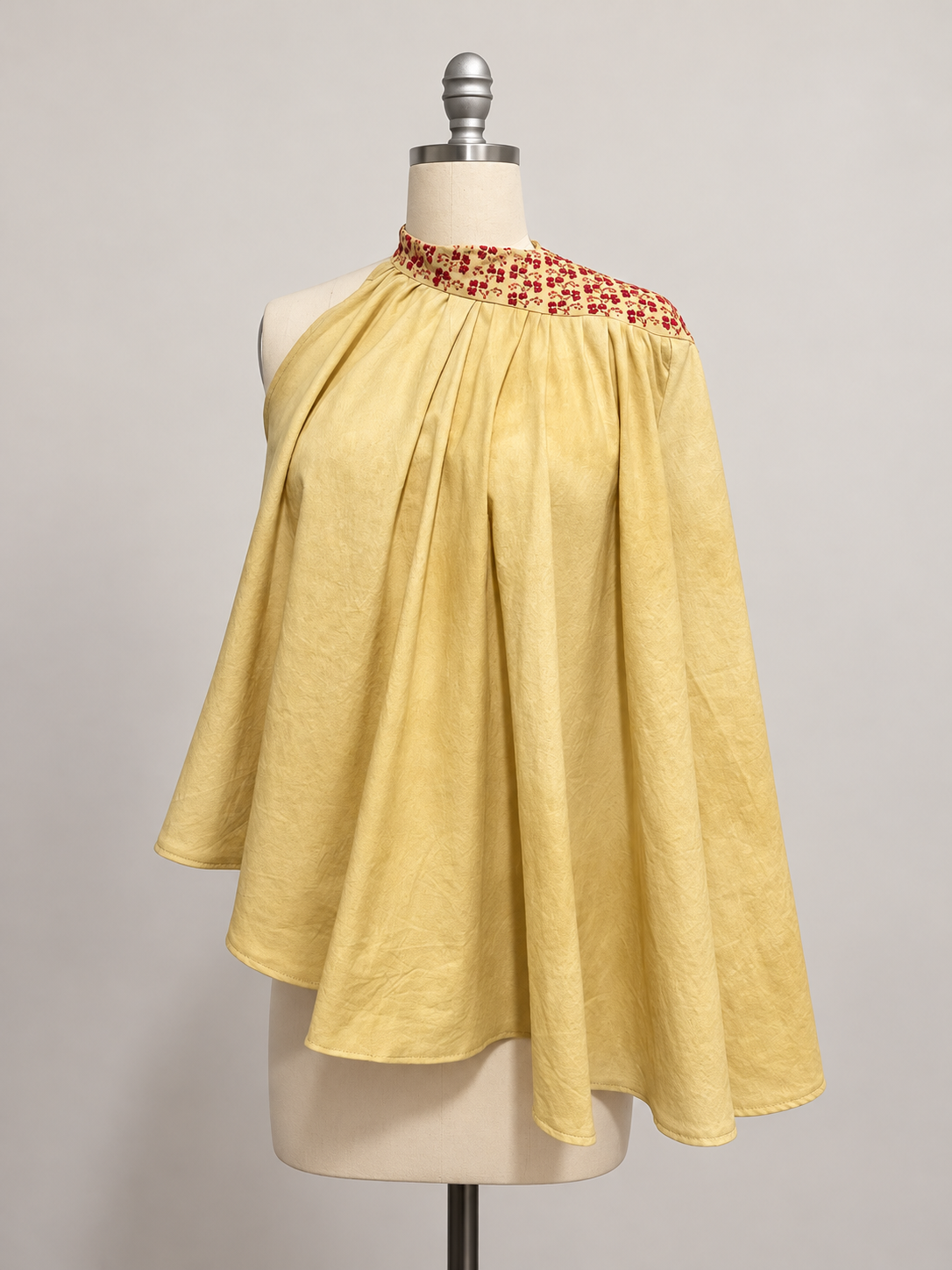 Yellow asymmetrical draped cape top with red Palestinian embroidery around the neckline, displayed on a mannequin.