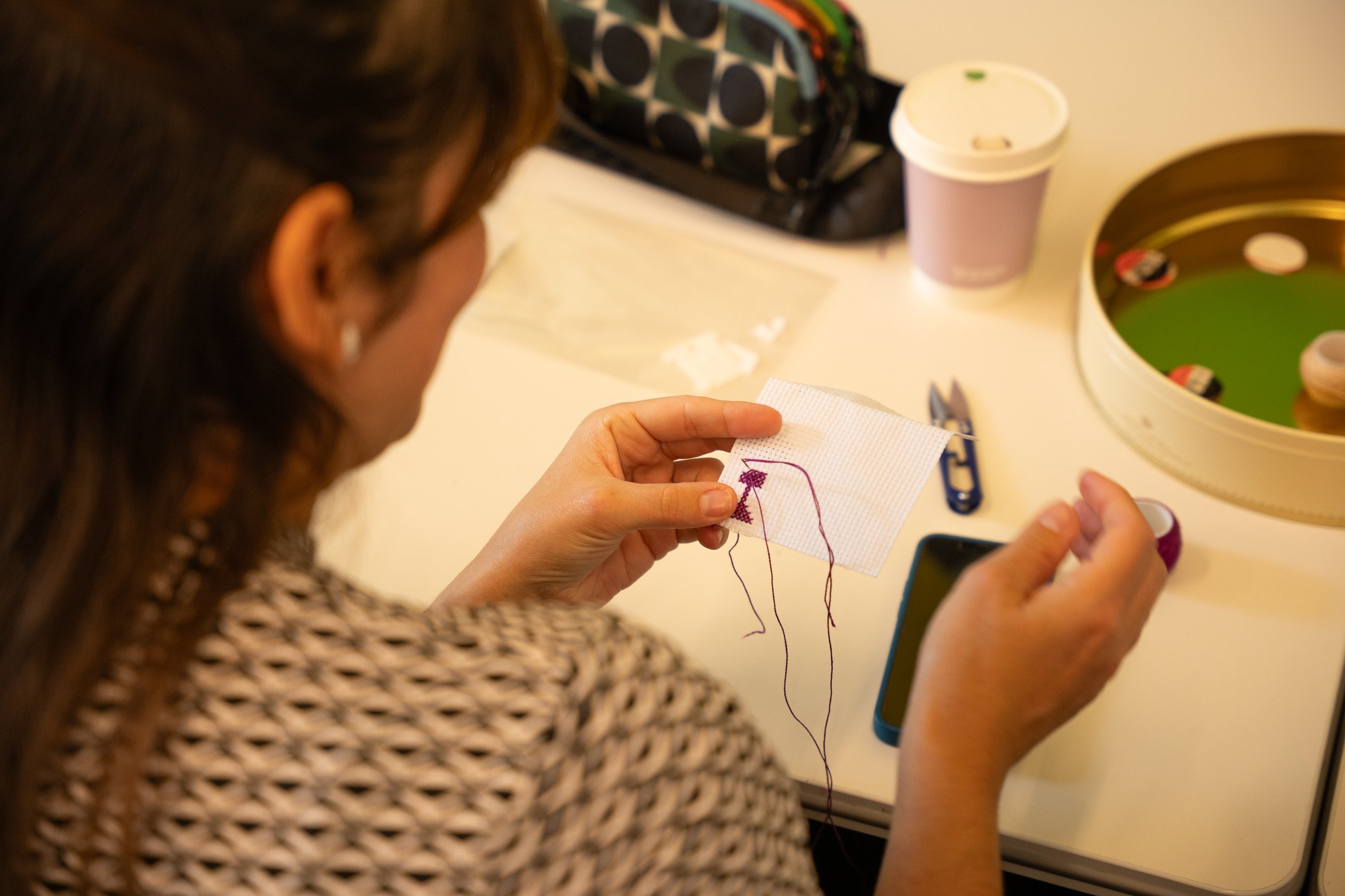 Participant stitching a purple Palestinian tatreez cross-stitch motif onto white Aida fabric during a hands-on embroidery workshop.