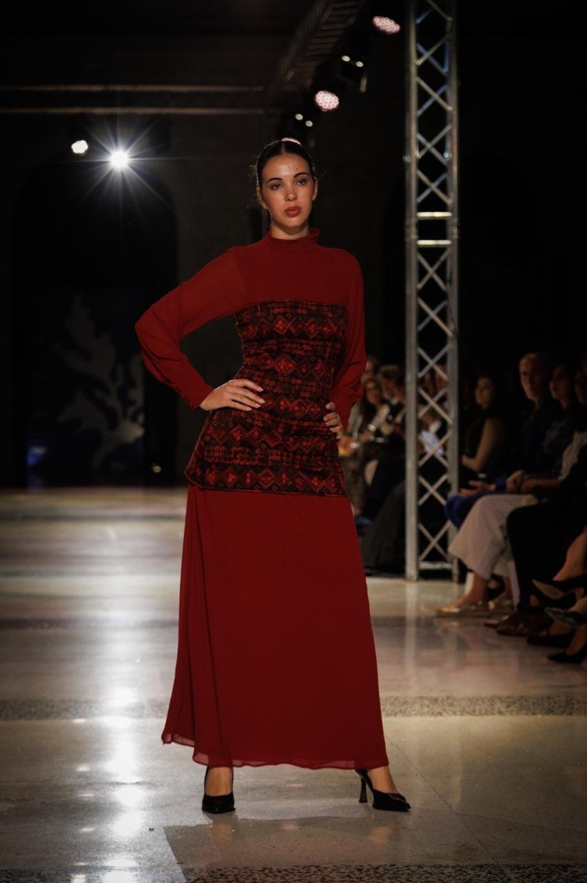 Model wearing a burgundy dress with a dark red Palestinian embroidered bodice at The Tatreez Collective fashion show.