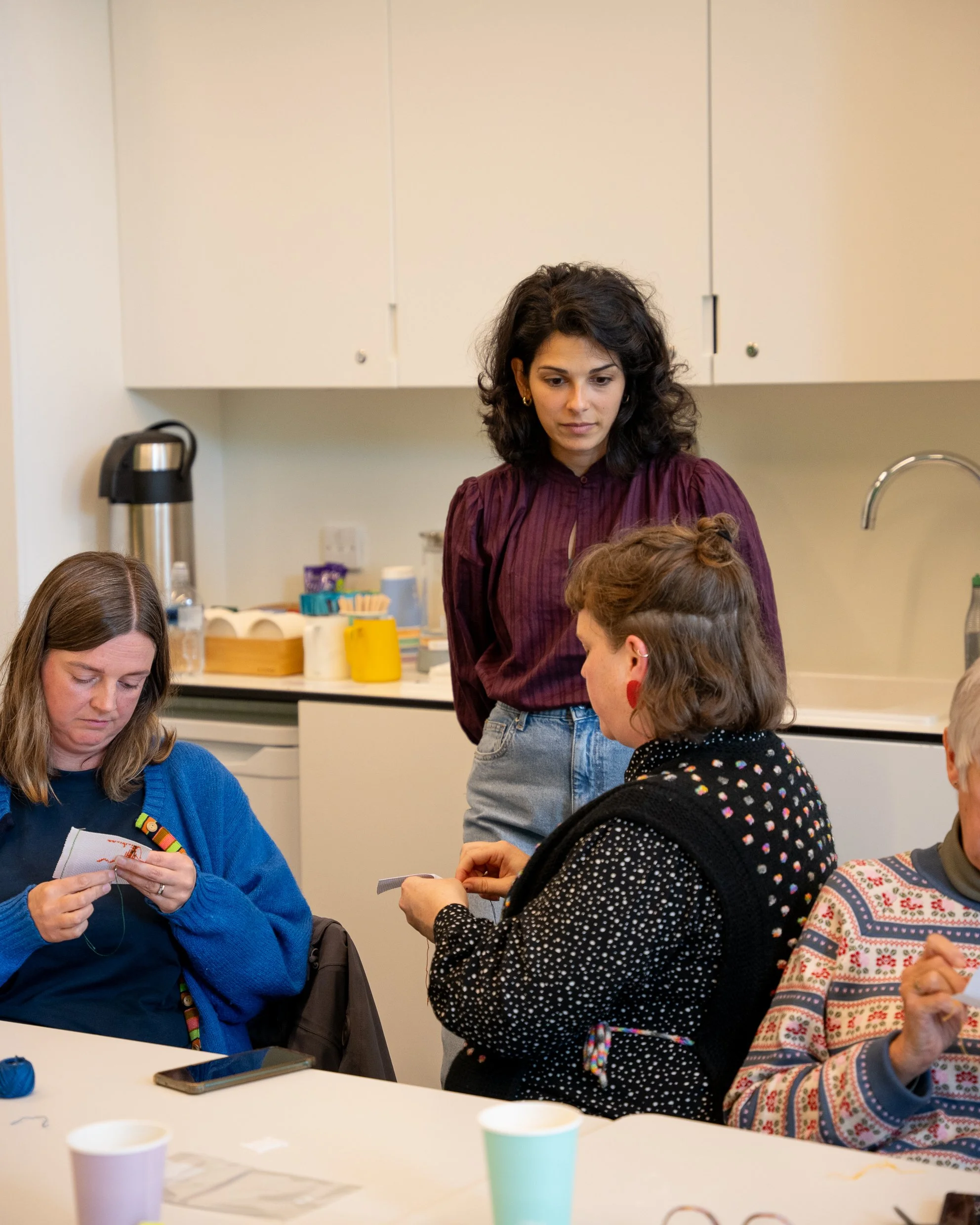 A Tatreez Collective facilitator supporting participants as they learn Palestinian embroidery during a hands-on group workshop.