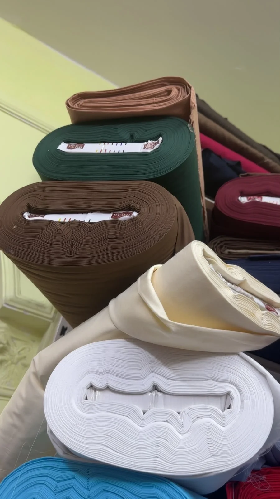 Rolls of fabric in brown, green, burgundy, cream and blue, selected for clothing production.