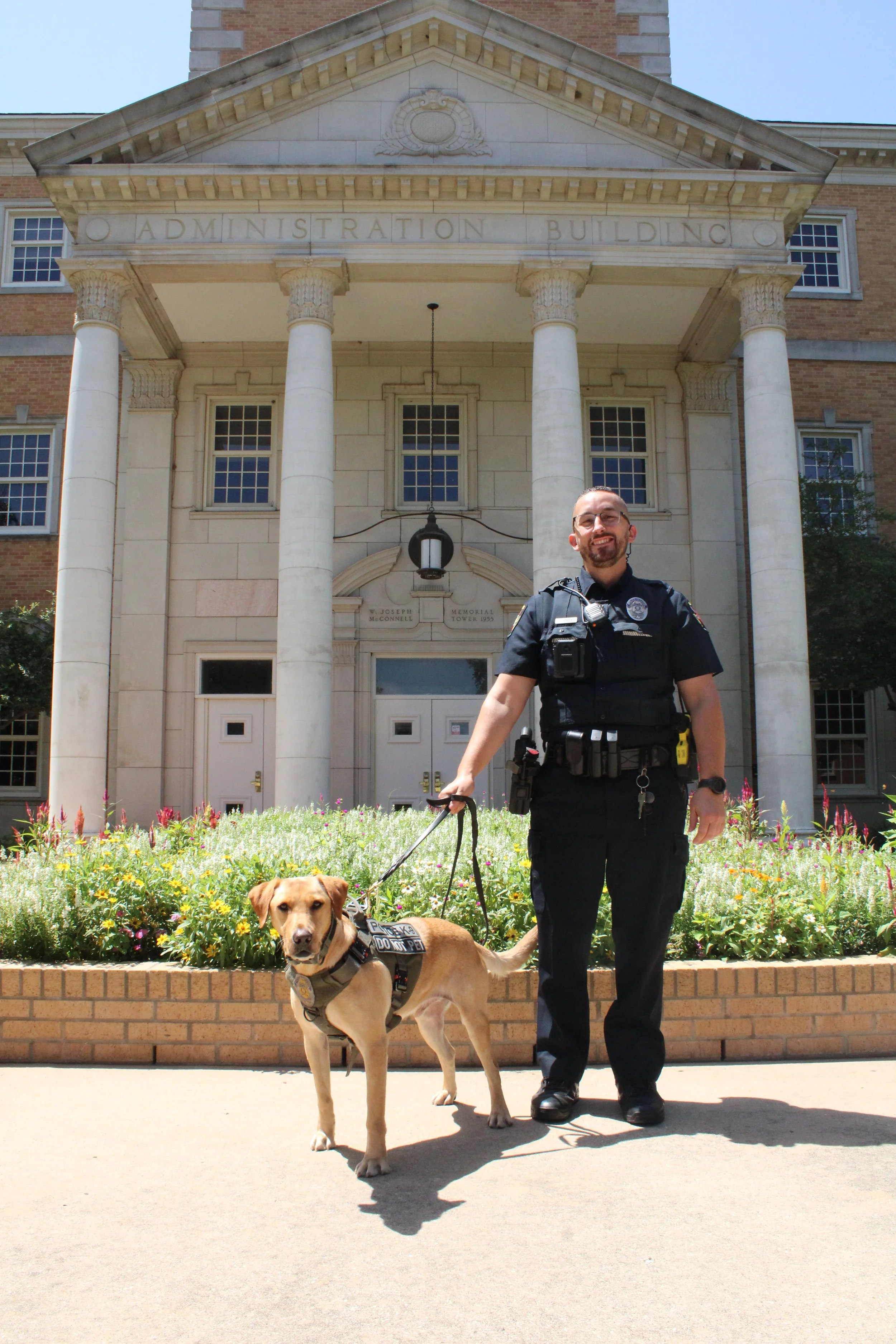 UNT PD Officer Cioffi and K-9, Watson standing in front of the Hurley Administration Building.