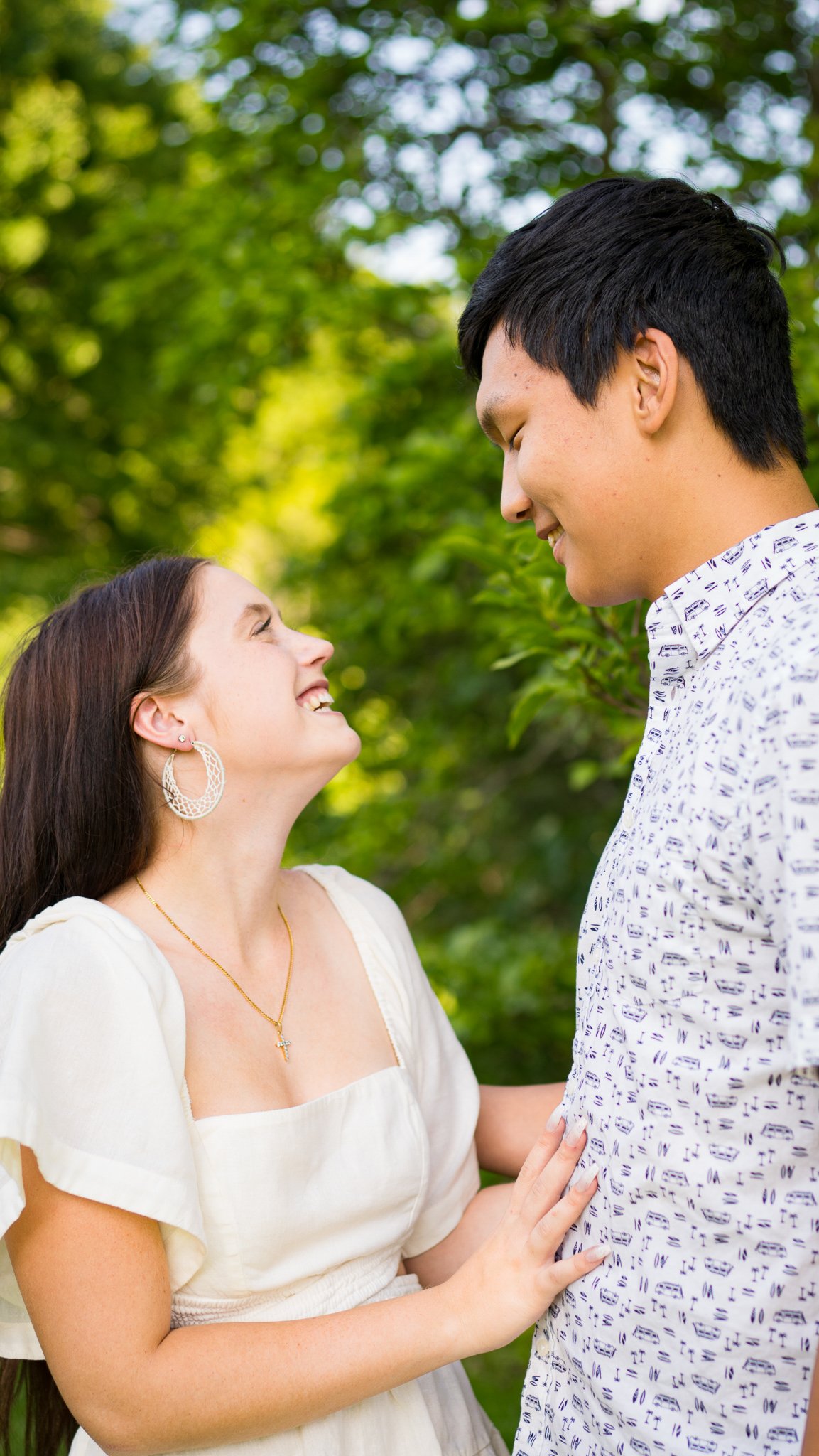 A woman and a man are smiling and looking at each other in a garden with lush greenery.