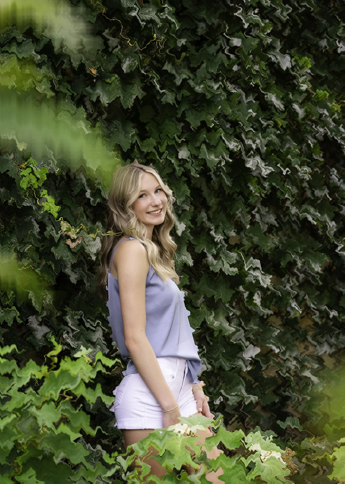 Young woman with blonde wavy hair wearing a light blue top and white shorts, smiling, standing outdoors near green foliage, with an artistic, distorted background.