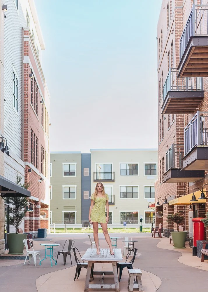 A woman standing on a table in an outdoor courtyard surrounded by modern apartment buildings.