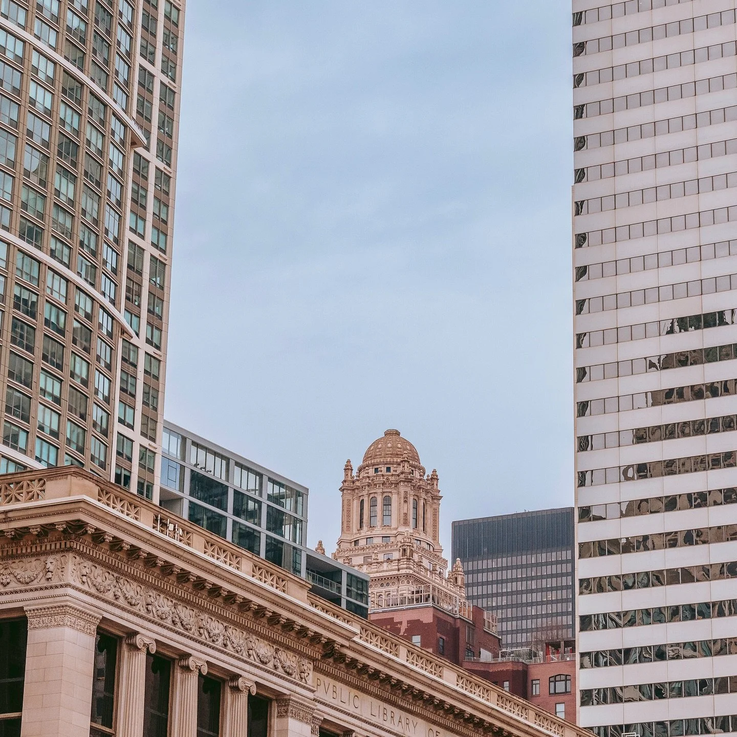View of tall modern office buildings surrounding an ornate historic building with a dome, in an urban cityscape.