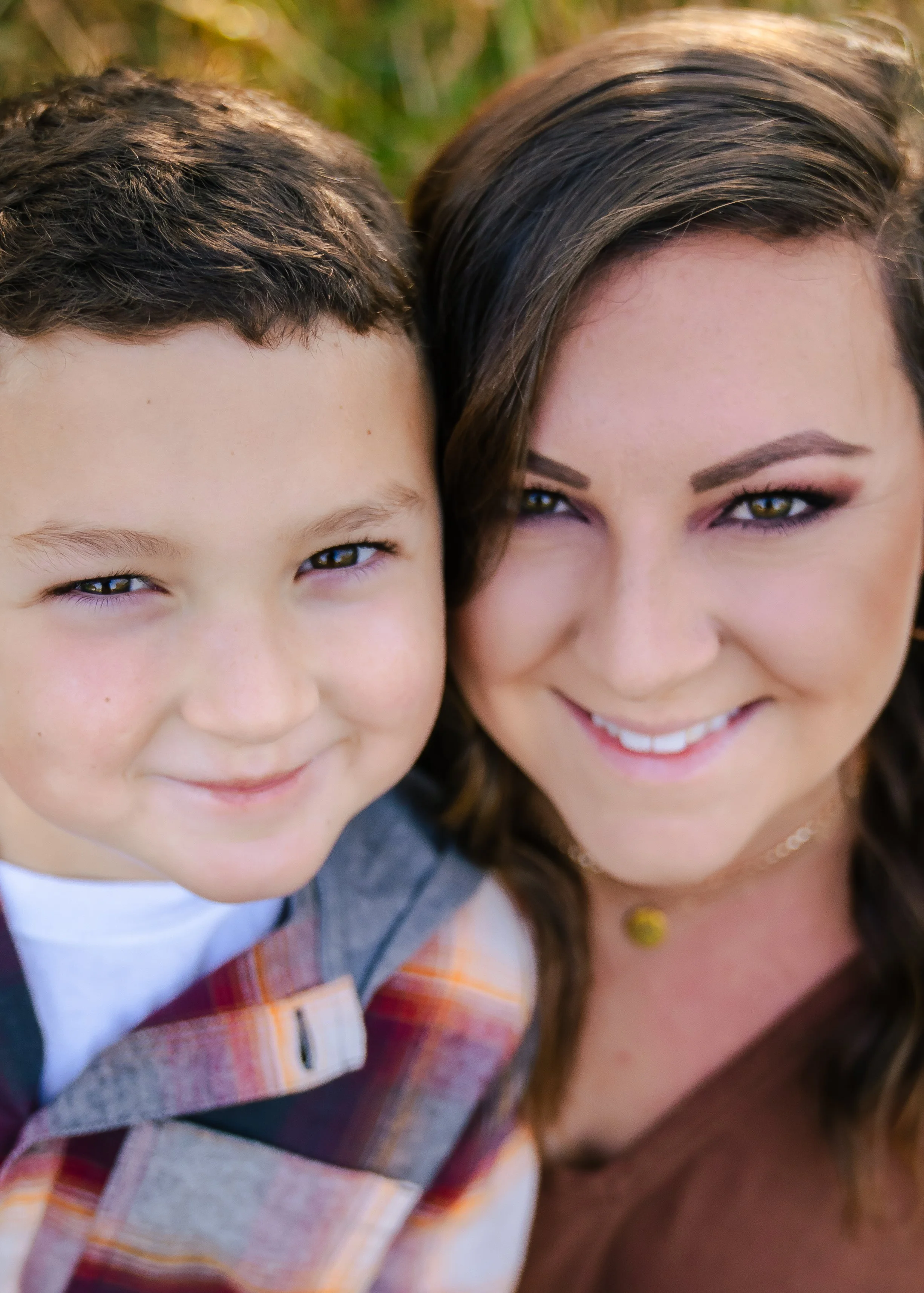 Close-up of a smiling woman and young boy outdoors, both facing the camera.