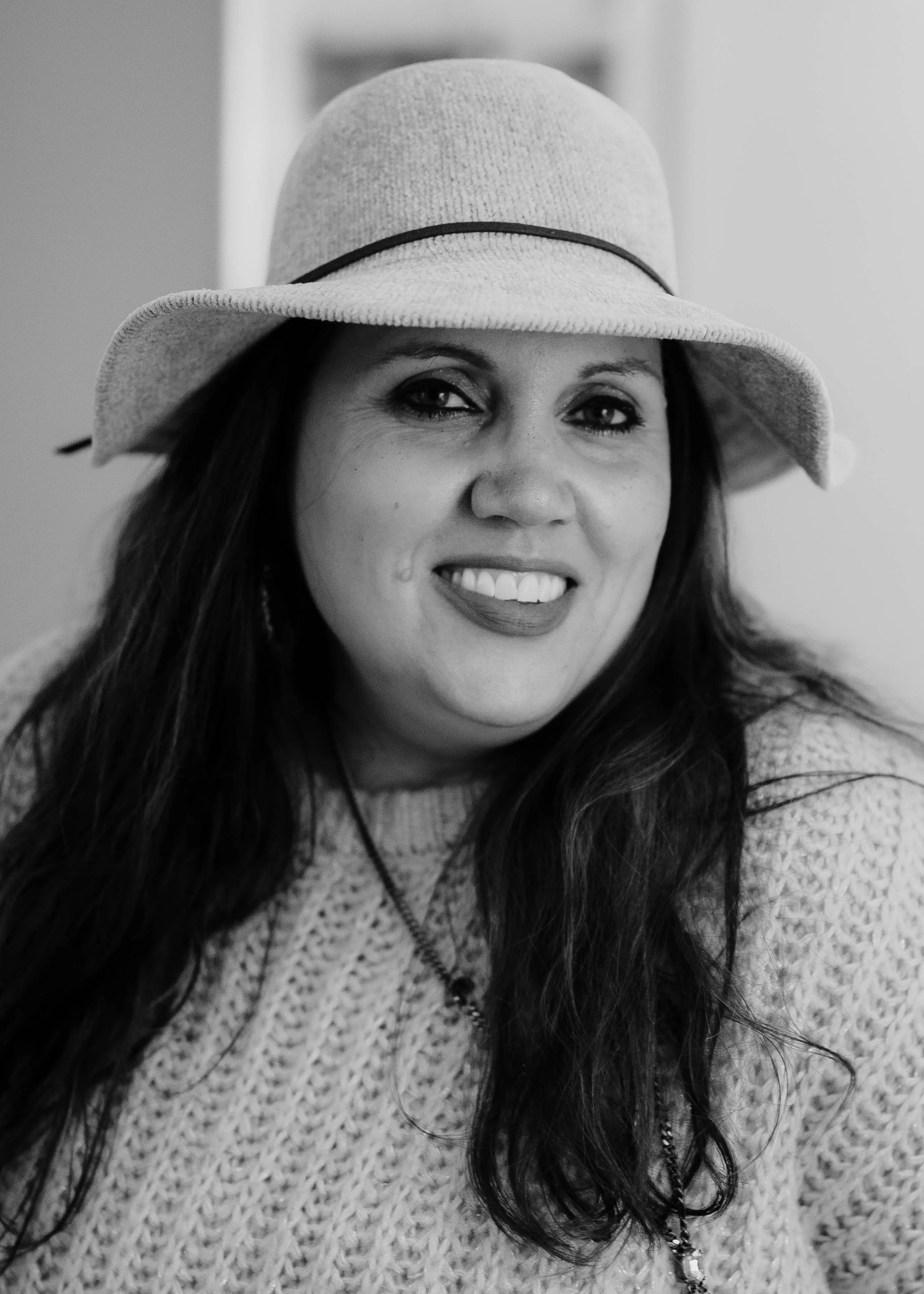 A woman wearing a wide-brimmed hat and a knit sweater, smiling at the camera.