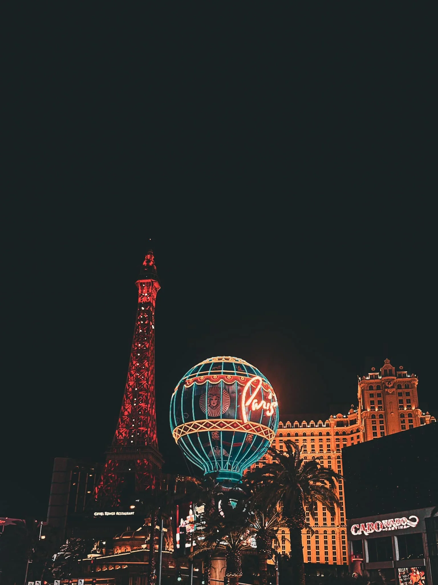 Night view of Las Vegas Strip with illuminated Paris Las Vegas hotel sign, Paris Tower replica, and surrounding buildings.