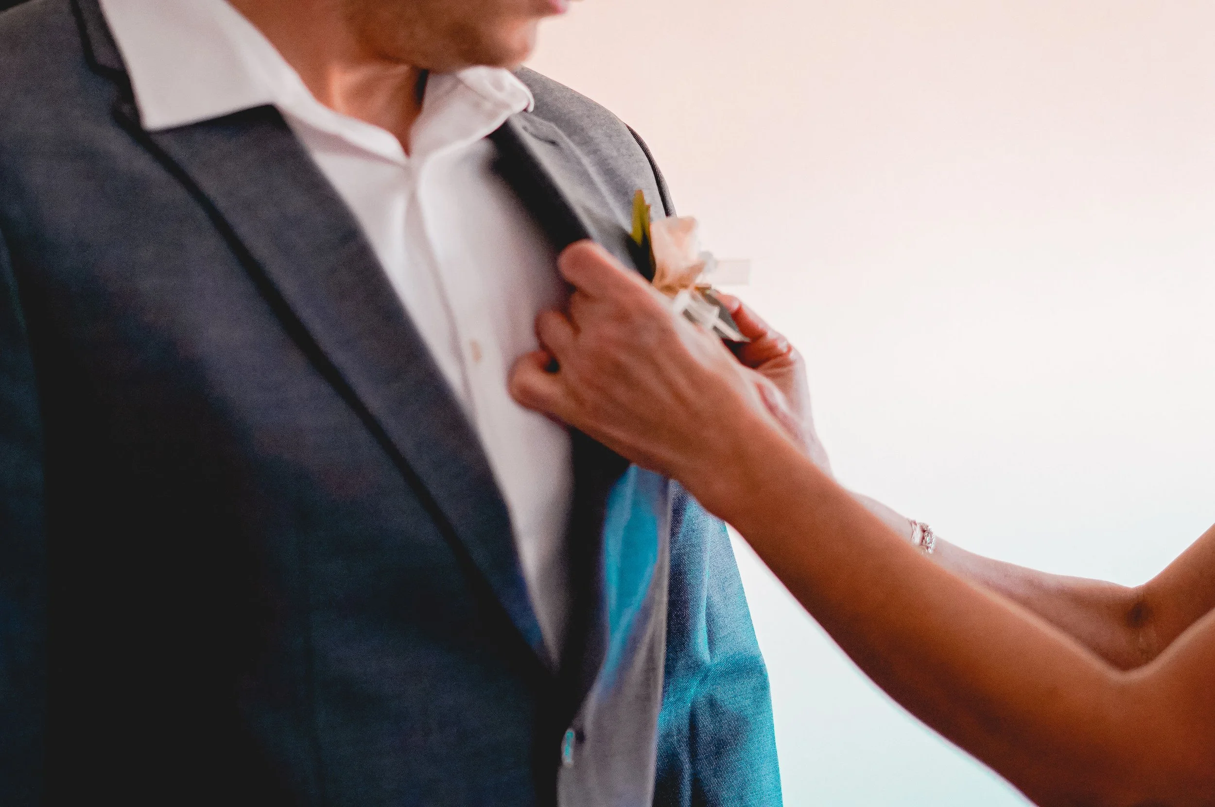 A person pinning a boutonniere onto a man's blazer.