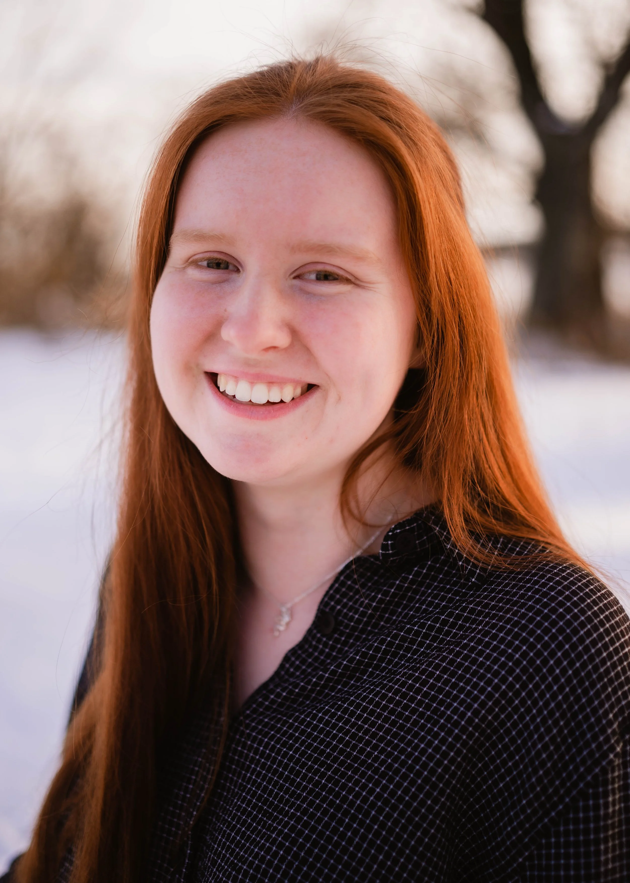 A young woman with long red hair smiling outdoors in a snowy landscape.