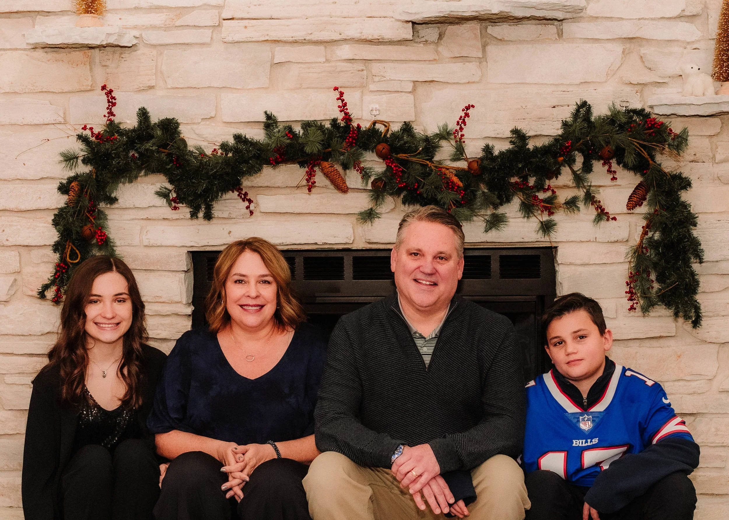A family of four sitting in front of a fireplace decorated with a Christmas garland, smiling at the camera.