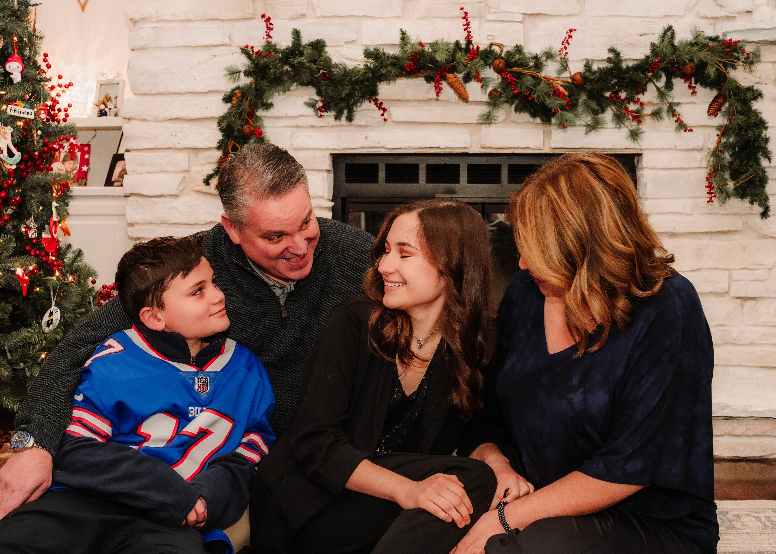 Family gathered by the fireplace decorated with holiday garland and a Christmas tree, sharing a joyful moment during Christmas.