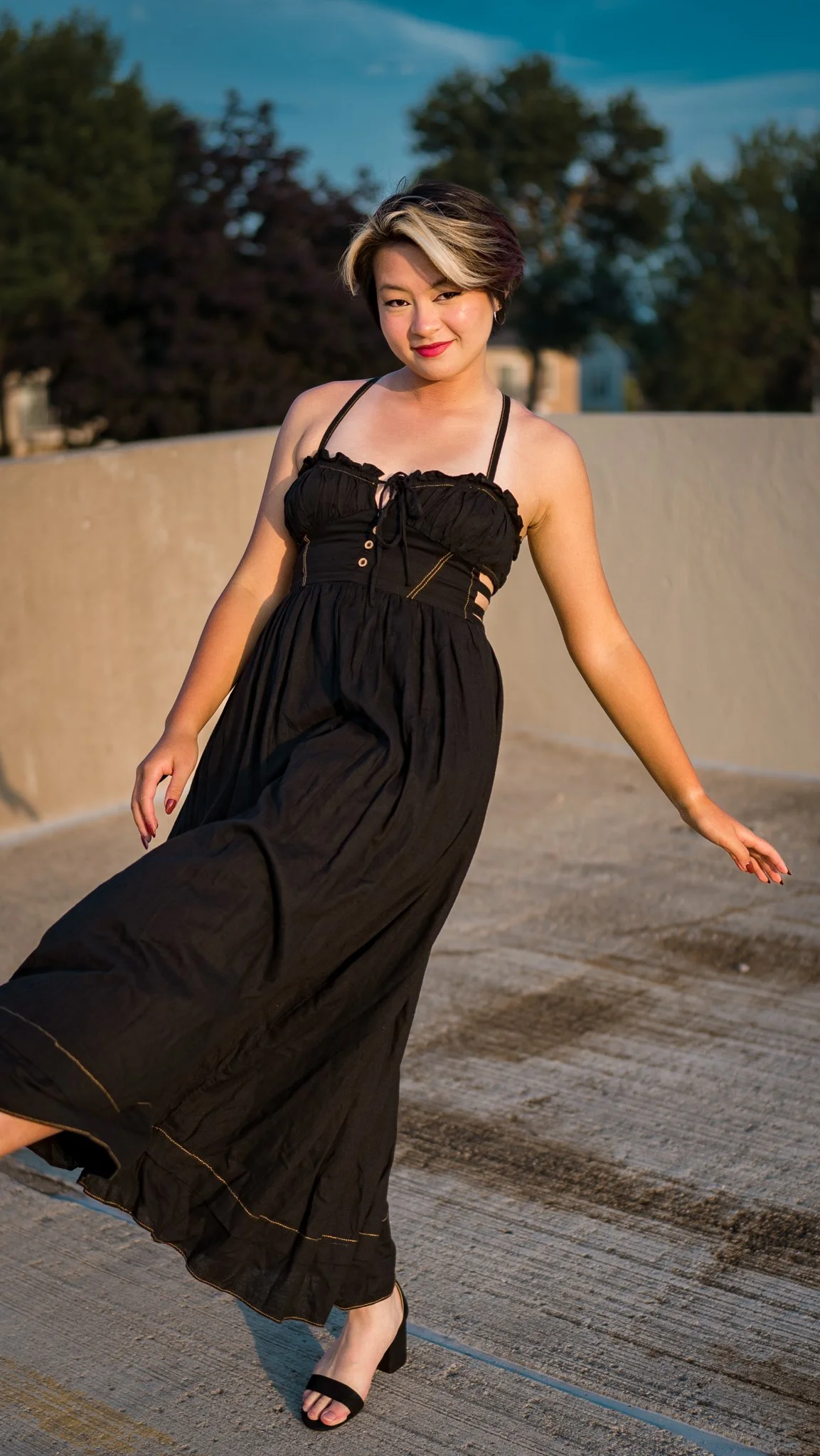 Woman in a black dress posing outdoors on a sunny day.