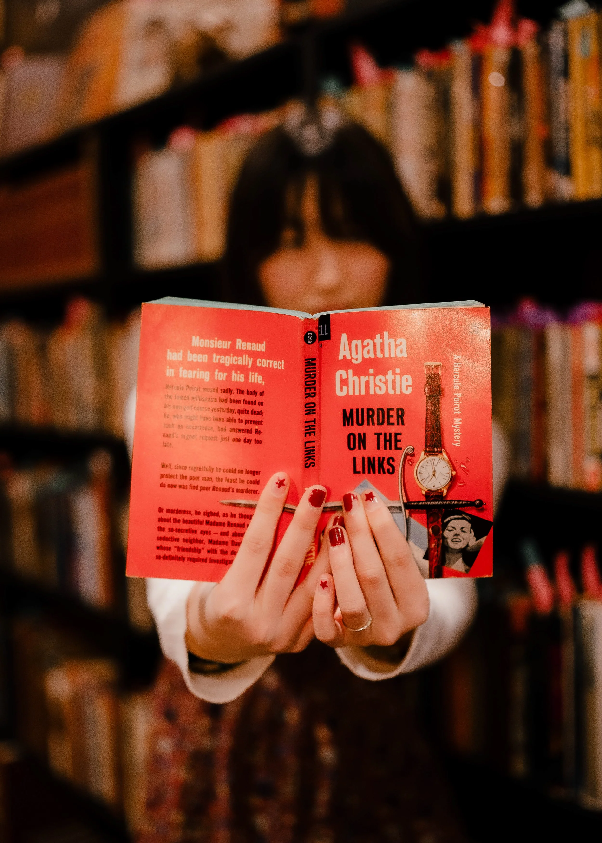 Person holding an open book titled 'Murder on the Links' by Agatha Christie in a library, with bookshelves filled with books in the background.