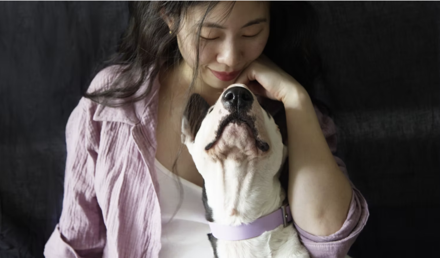 Woman gently hugging a dog with closed eyes and a peaceful expression.