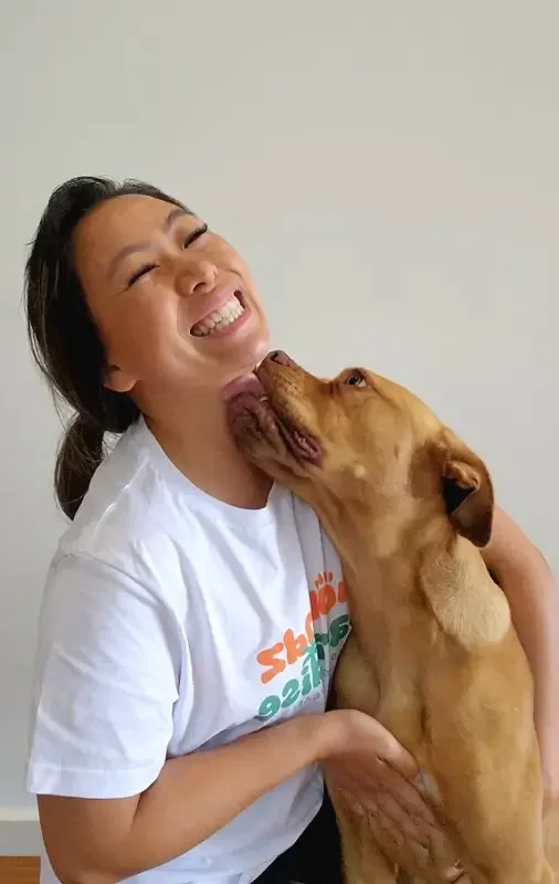 Woman smiling as brown dog licks her chin