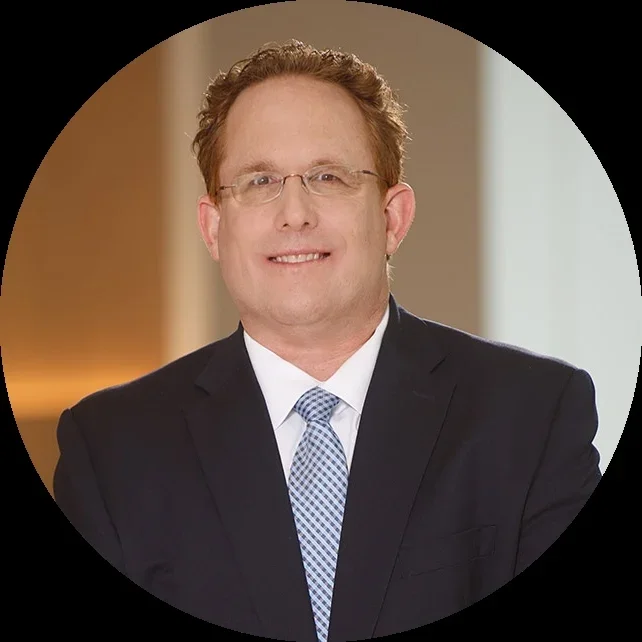 A smiling man in a business suit standing in an office with arms crossed.