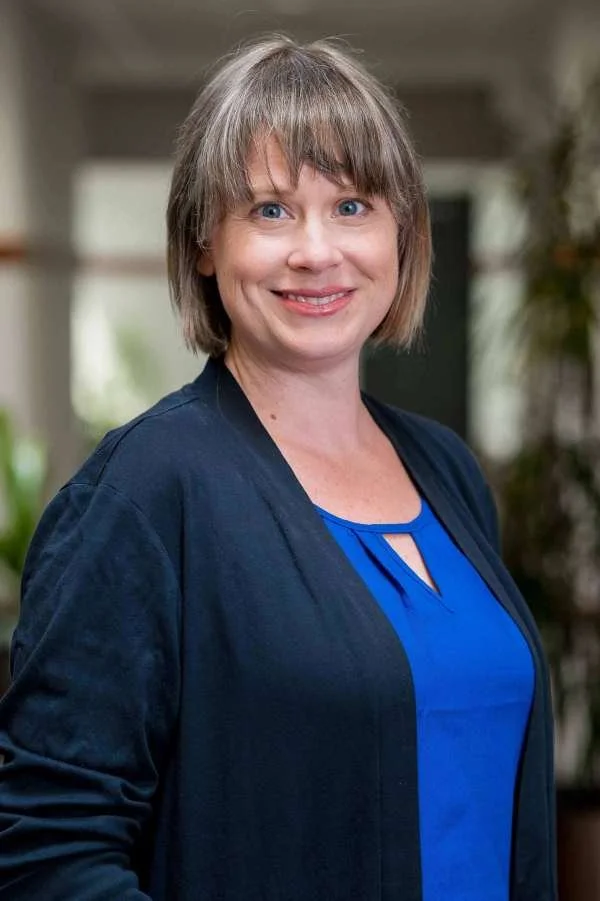 Woman with short hair smiling posing for a photo wearing blue
