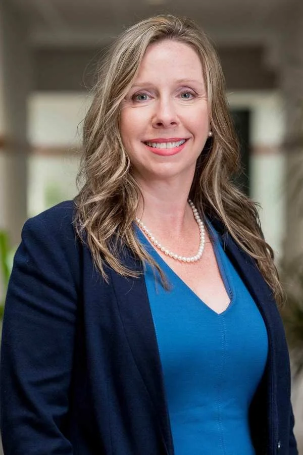 A woman smiling with necklace and blue shirt