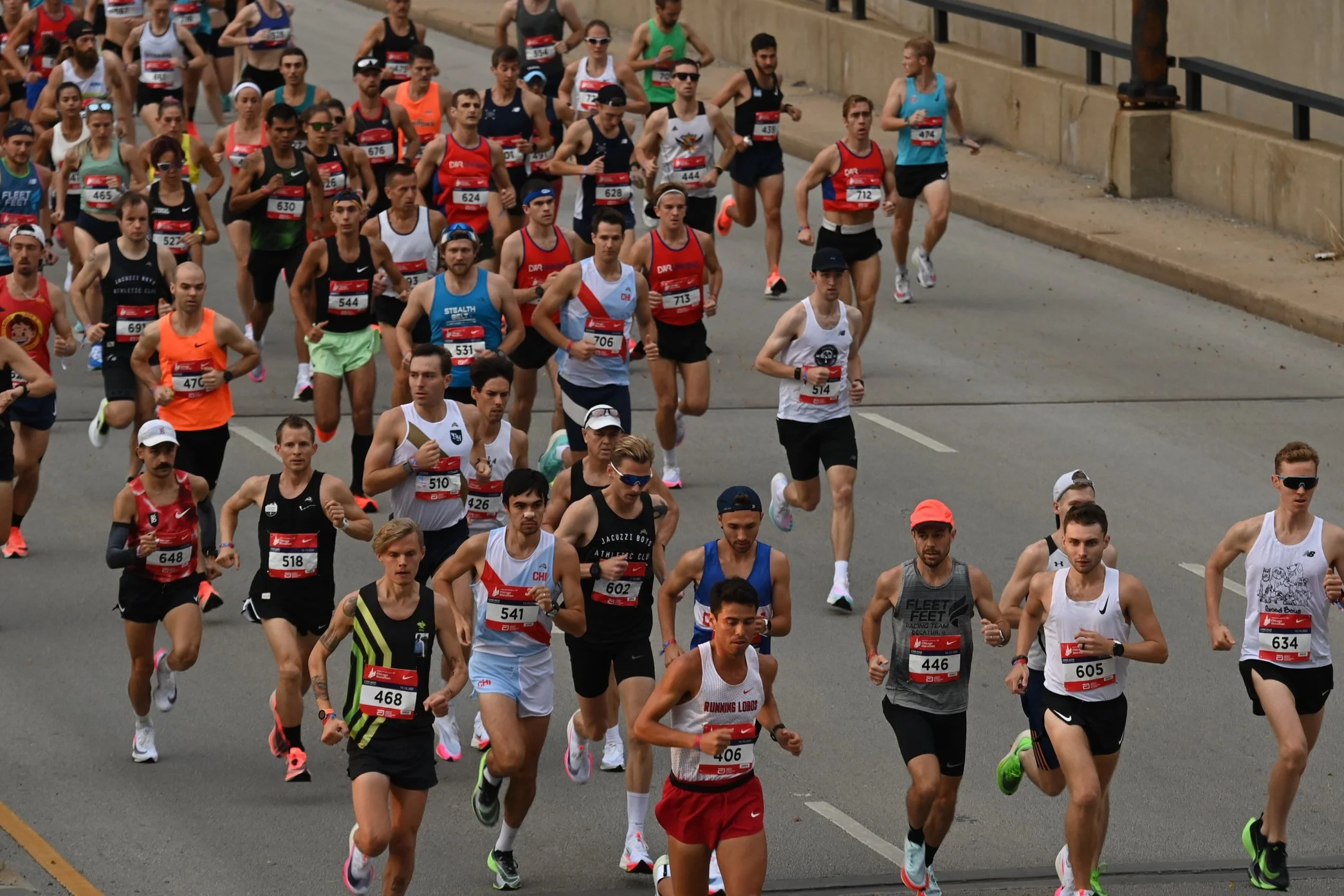 A large group of runners participating in a marathon on a city street, wearing athletic gear and race bibs.