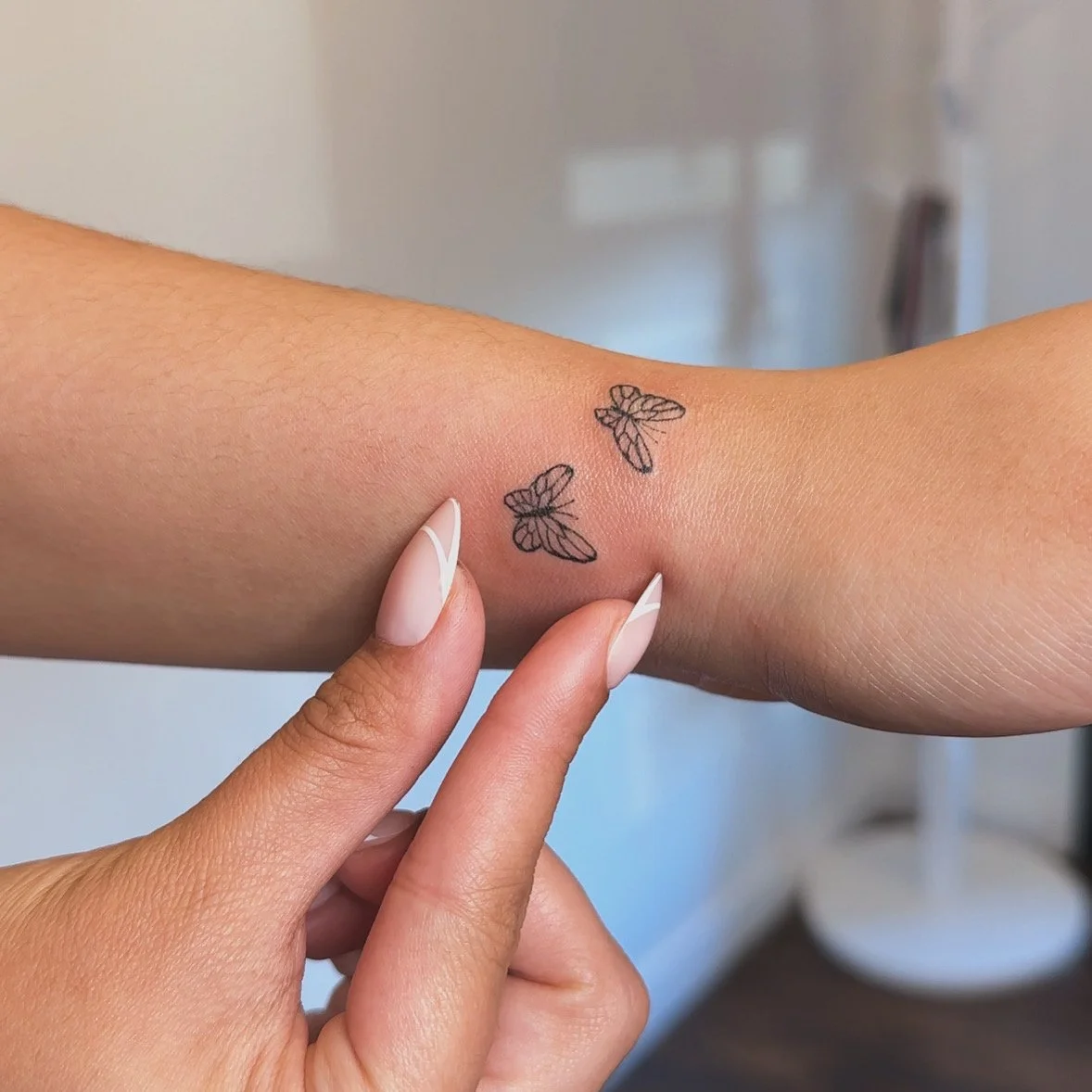 Close-up of a person's wrist with two small butterfly tattoos in Los Angeles Fine Line
