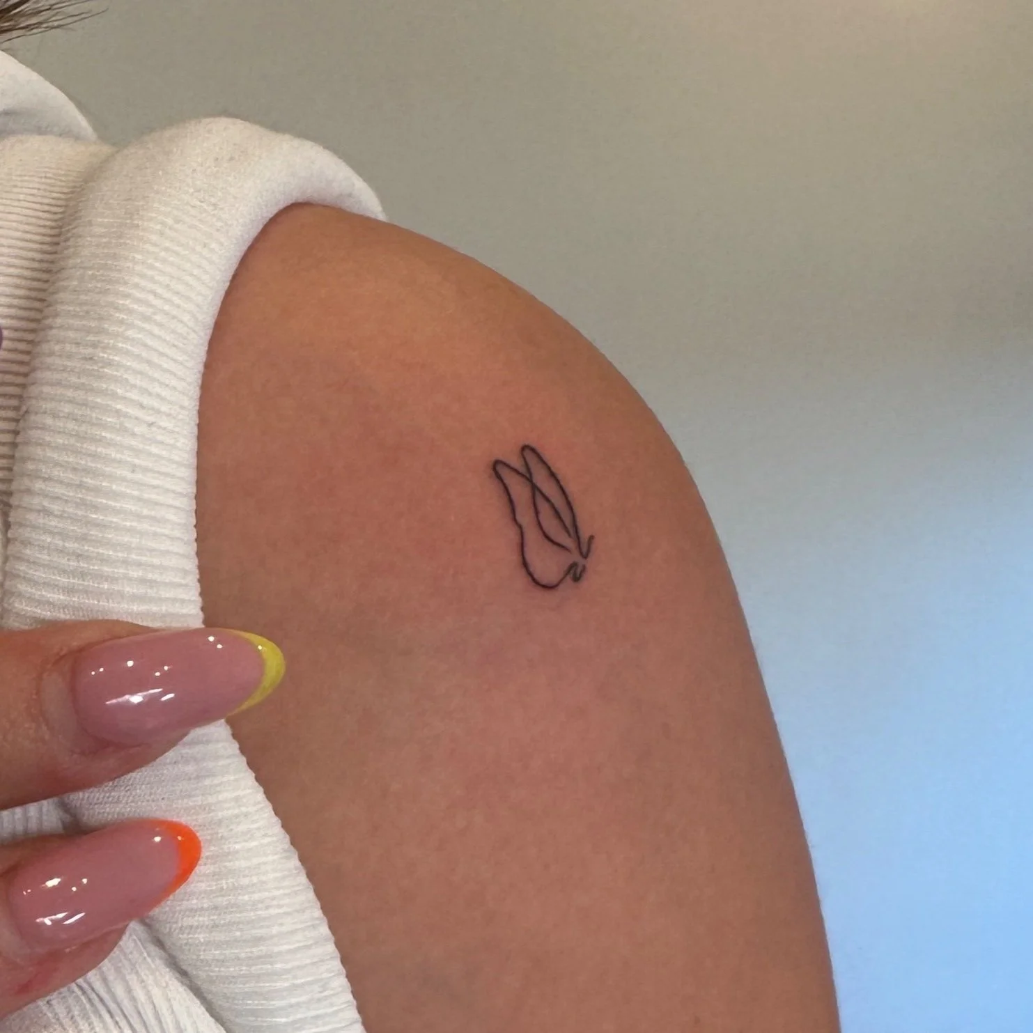 tiny tattoos of a butterfly on an upper arm next to a hand with colorful French manicure in Los Angeles
