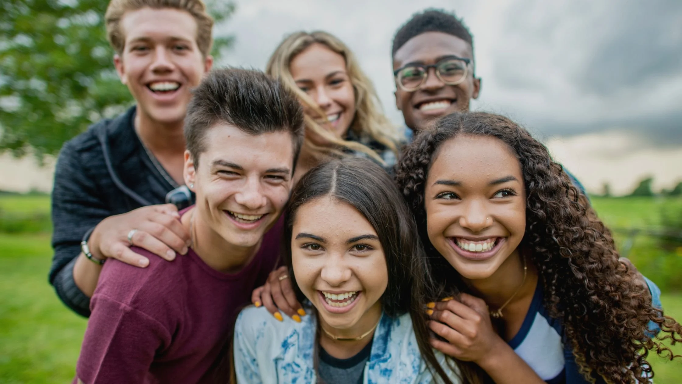 Group of smiling young people outdoors in a park, close-up shot.