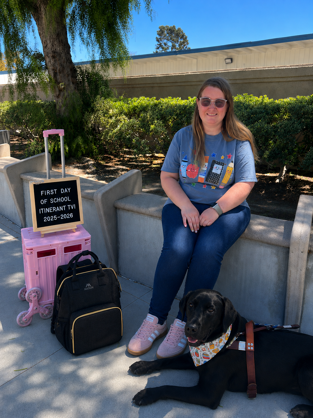 Lindsay sitting on a bench with her teaching supplies next to her. Eve is also laying on the oposite side in harness with a school themed bandana on.