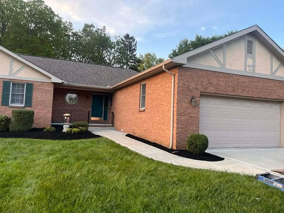 Front view of a brick and siding house with a manicured lawn and a newly landscaped garden bed.