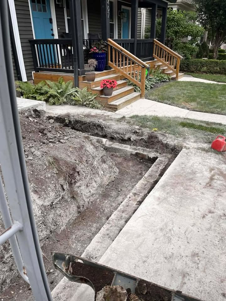 Front porch of a house with steps, potted plants, and a new wooden railing, while the front yard is under construction with exposed dirt and concrete sidewalk.