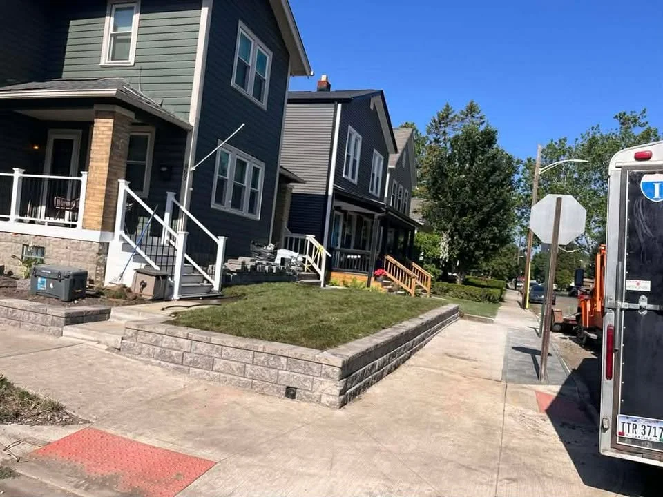 Row of modern houses on a sunny day with a sidewalk, grass, trees, and a parked truck.