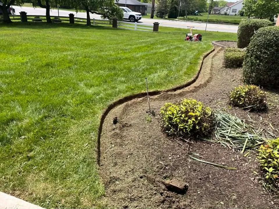 A landscaped front yard with freshly dug flower beds along the edge of a well-maintained lawn, with a string line marking the border of the beds.