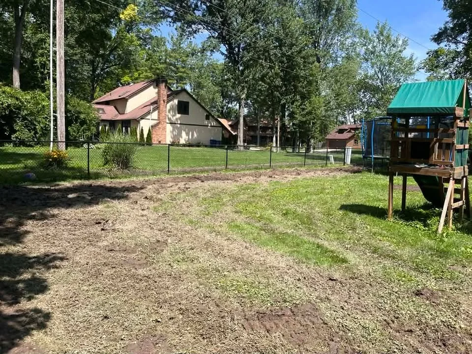 Backyard with a fenced grassy area, a wooden playhouse, trees, and neighboring houses.