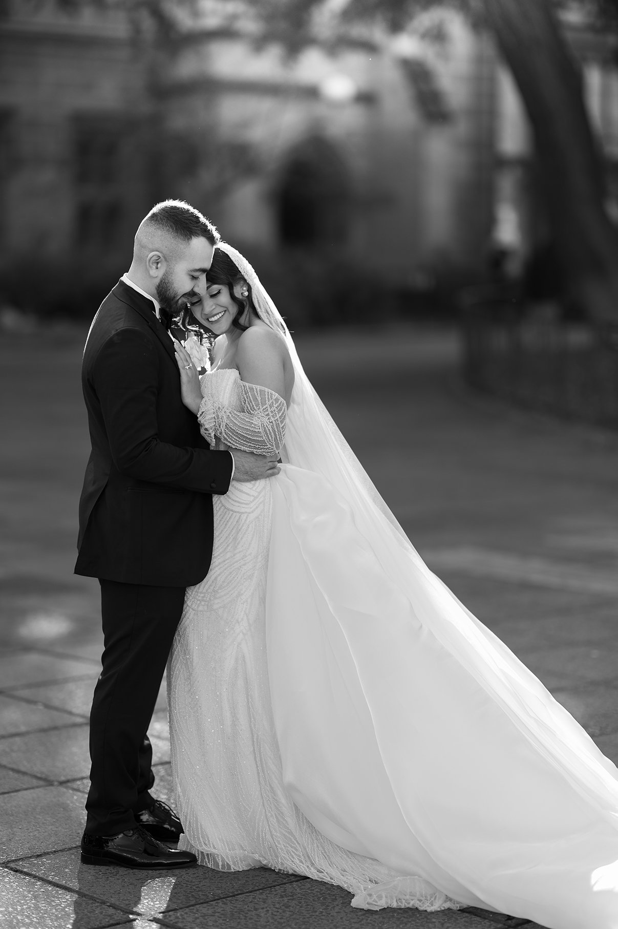 A tender photo captured at Melbourne University featuring the couple in an embracing hold, conveying a moment of closeness and affection. The old building in the background is artfully blurred out, focusing attention on the couple's intimate interact